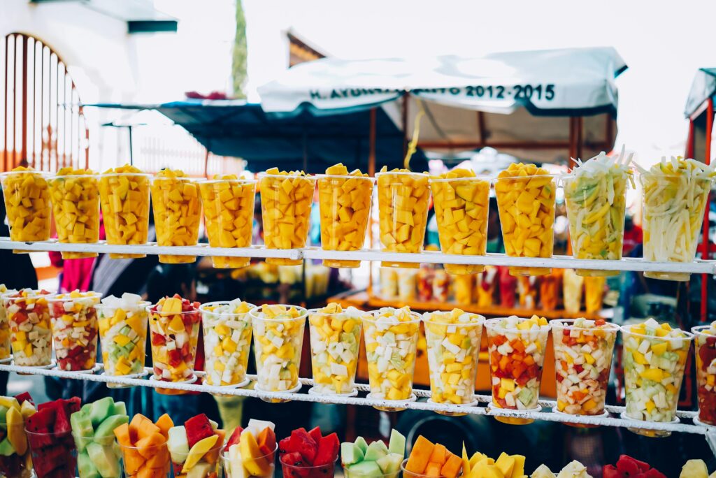 Vibrant display of fresh fruit cups at a sunny outdoor market.